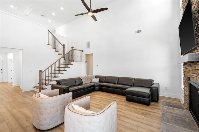 living room featuring ceiling fan, a towering ceiling, a fireplace, and light wood-type flooring