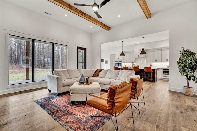 living room with sink, beam ceiling, light hardwood / wood-style floors, and a high ceiling