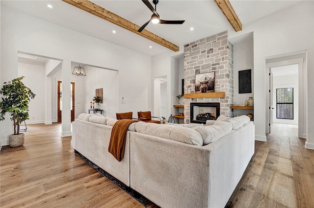 living room with beam ceiling, a stone fireplace, ceiling fan, and light wood-type flooring