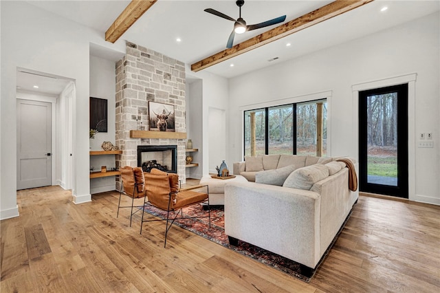 living room featuring beam ceiling, a stone fireplace, light hardwood / wood-style floors, and ceiling fan