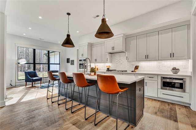 kitchen featuring white cabinetry, light wood-type flooring, appliances with stainless steel finishes, an island with sink, and pendant lighting