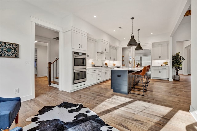 kitchen with white cabinetry, decorative backsplash, stainless steel appliances, and a center island with sink