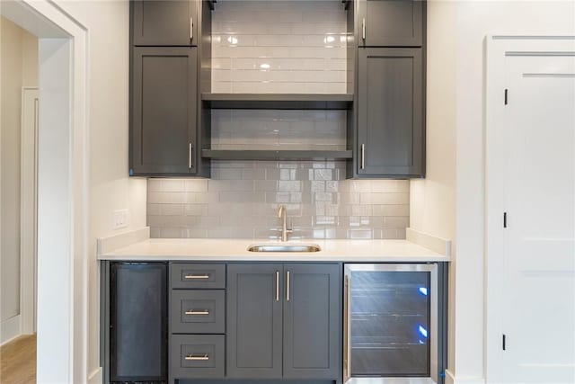 bar with tasteful backsplash, sink, gray cabinets, and beverage cooler