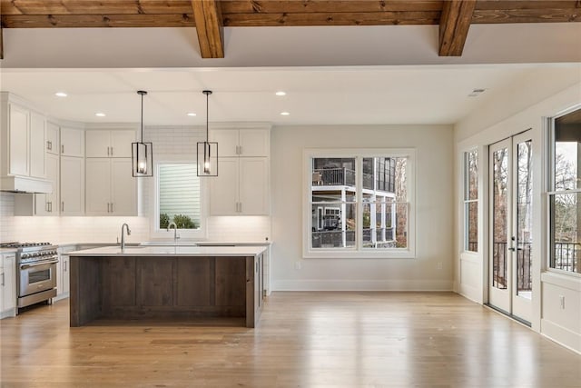 kitchen featuring hanging light fixtures, beam ceiling, tasteful backsplash, high end stainless steel range, and a center island with sink