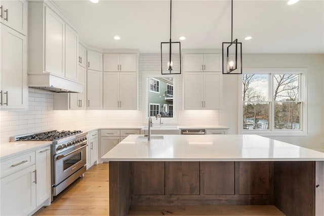 kitchen with stainless steel range, decorative light fixtures, white cabinets, and a center island with sink