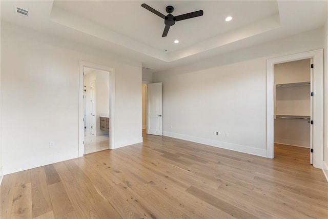 unfurnished bedroom with connected bathroom, a walk in closet, light hardwood / wood-style floors, a tray ceiling, and a closet