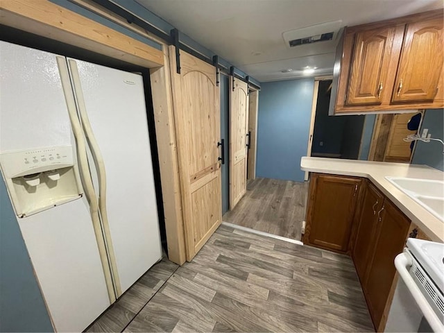 kitchen featuring dark hardwood / wood-style flooring, a barn door, sink, and white appliances