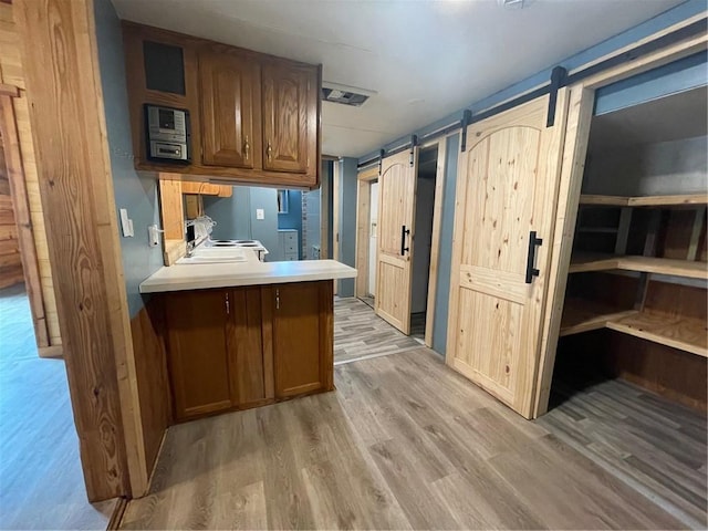 kitchen with sink, light hardwood / wood-style floors, a barn door, and kitchen peninsula