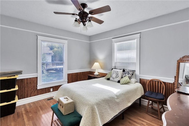 bedroom with hardwood / wood-style floors, wooden walls, and ceiling fan