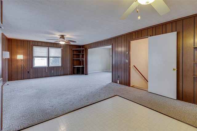 interior space featuring a textured ceiling, wooden walls, ceiling fan, and carpet