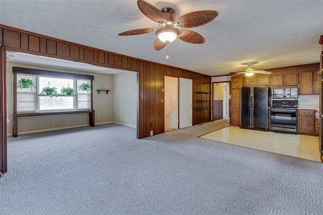 kitchen with light colored carpet, ornamental molding, wooden walls, ceiling fan, and black appliances