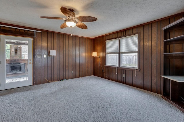 spare room featuring ceiling fan, carpet flooring, wooden walls, and a textured ceiling