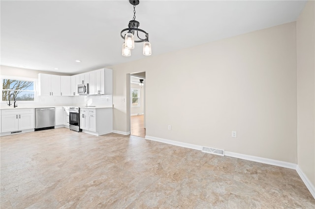 kitchen with appliances with stainless steel finishes, pendant lighting, white cabinetry, sink, and decorative backsplash