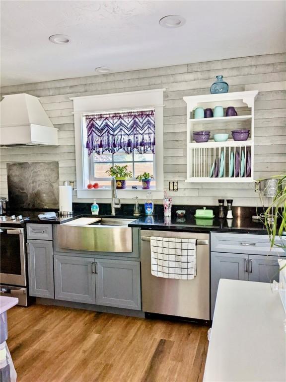 kitchen with gray cabinets, sink, stainless steel appliances, custom range hood, and light wood-type flooring