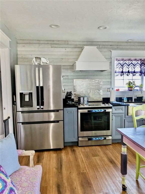 kitchen with sink, light hardwood / wood-style flooring, premium range hood, gray cabinetry, and stainless steel appliances