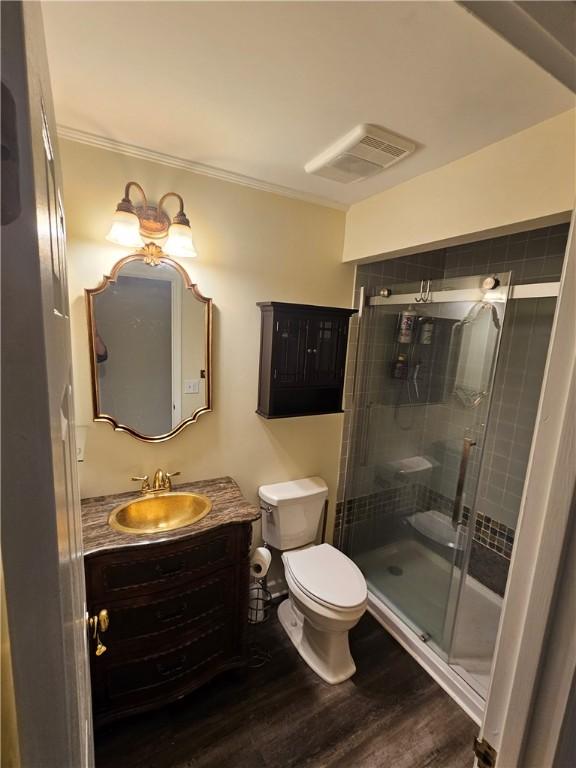 bathroom with toilet, a shower with shower door, wood-type flooring, ornamental molding, and vanity