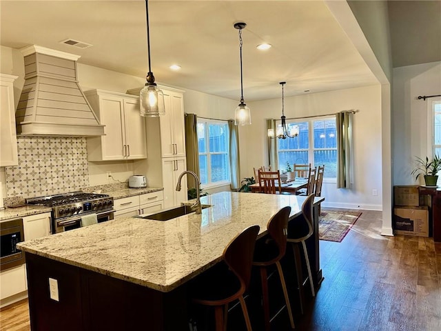 kitchen featuring appliances with stainless steel finishes, white cabinetry, sink, custom exhaust hood, and a kitchen island with sink