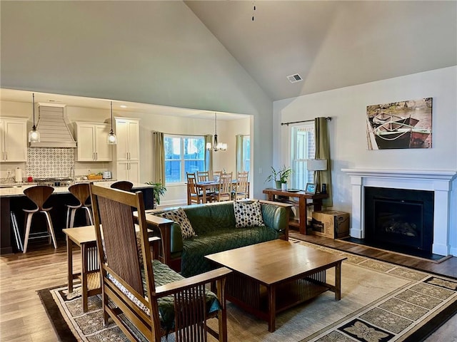 living room with light hardwood / wood-style flooring, high vaulted ceiling, and a chandelier