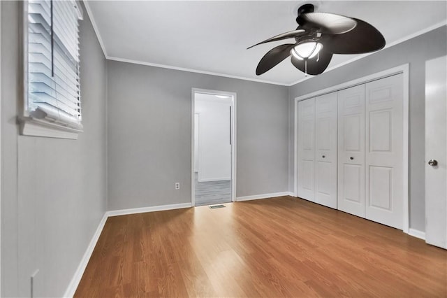 unfurnished bedroom with ornamental molding, ceiling fan, light wood-type flooring, and a closet