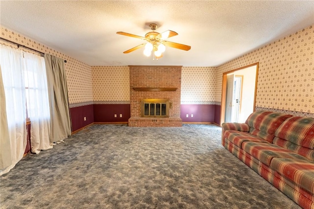 living room with a brick fireplace, ceiling fan, a textured ceiling, and dark colored carpet