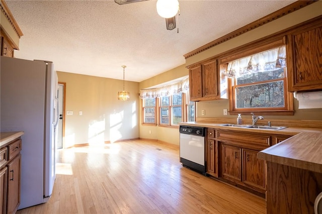 kitchen featuring sink, dishwasher, white refrigerator, decorative light fixtures, and light wood-type flooring