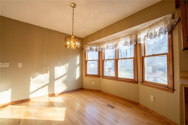 unfurnished dining area with hardwood / wood-style floors, a notable chandelier, and a textured ceiling