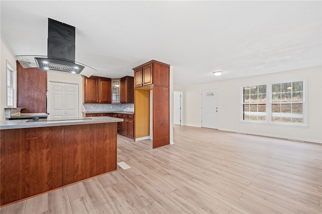 kitchen featuring backsplash, black electric stovetop, island exhaust hood, kitchen peninsula, and light wood-type flooring