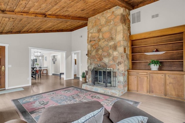 living room featuring beamed ceiling, a stone fireplace, light wood-type flooring, and wooden ceiling