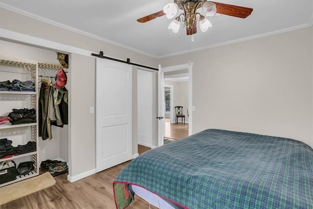 bedroom with ceiling fan, ornamental molding, a barn door, and light wood-type flooring