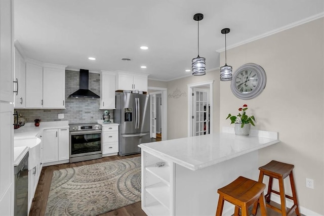 kitchen featuring wall chimney exhaust hood, a kitchen bar, white cabinetry, appliances with stainless steel finishes, and kitchen peninsula