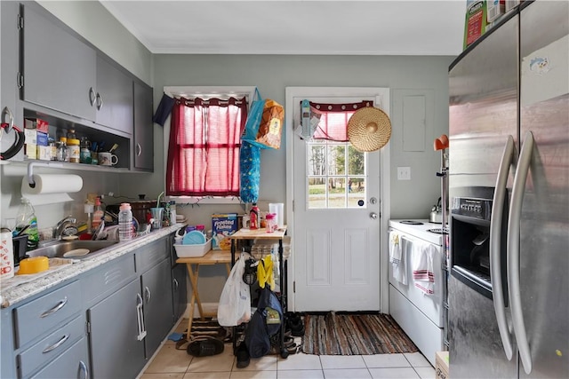 kitchen with light tile patterned floors, sink, gray cabinetry, stainless steel fridge with ice dispenser, and washer / dryer