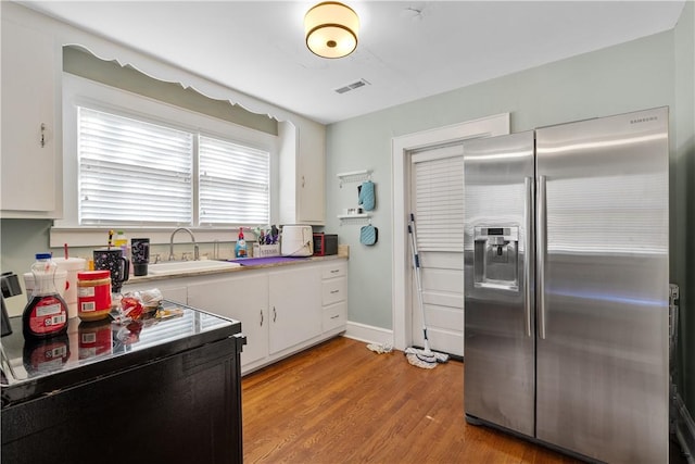 kitchen with white cabinetry, stainless steel refrigerator with ice dispenser, sink, and light hardwood / wood-style flooring