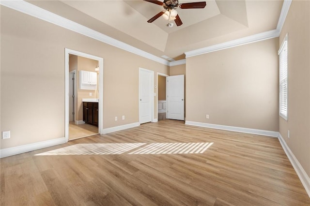 unfurnished bedroom featuring ornamental molding, connected bathroom, light wood-type flooring, and a tray ceiling