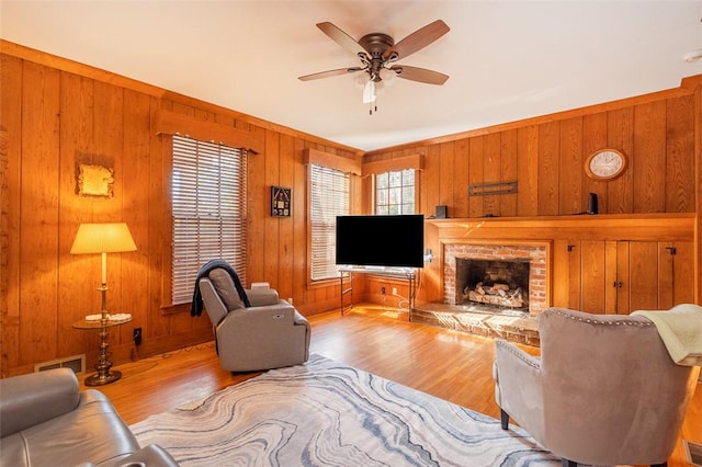 living room with wooden walls, ceiling fan, a fireplace, and light hardwood / wood-style floors