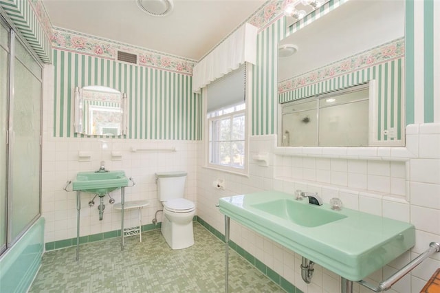 full bathroom featuring tile walls, sink, shower / bath combination with glass door, and toilet