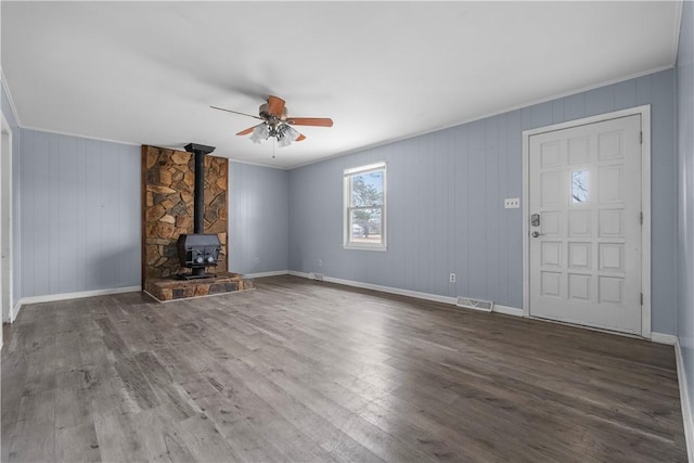 unfurnished living room with dark wood-type flooring, ornamental molding, ceiling fan, and a wood stove