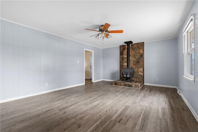 unfurnished living room featuring crown molding, a wood stove, dark wood-type flooring, and ceiling fan