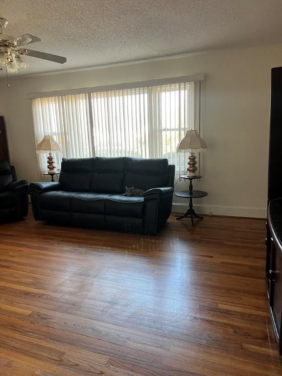 living room featuring ceiling fan, dark wood-type flooring, a wealth of natural light, and a textured ceiling