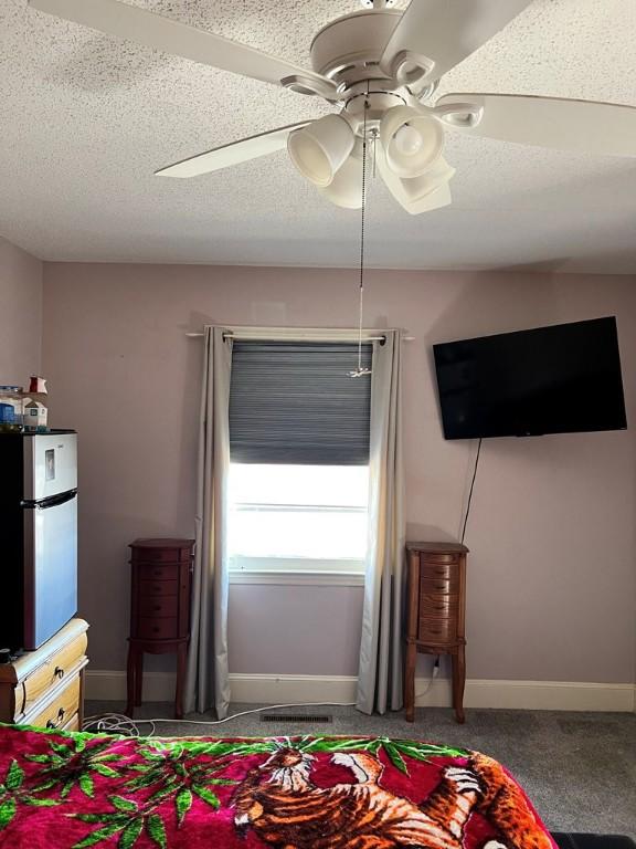 bedroom with ceiling fan, stainless steel refrigerator, a textured ceiling, and carpet flooring