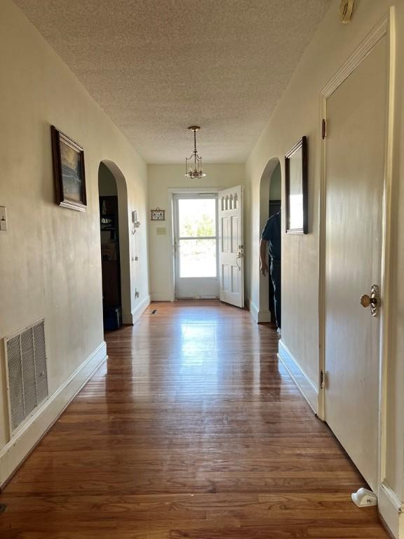 hall featuring hardwood / wood-style flooring, a textured ceiling, and a notable chandelier