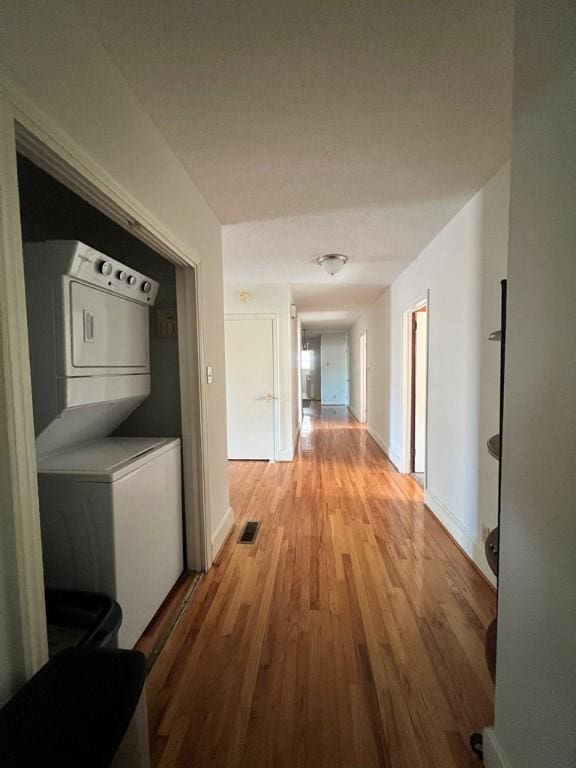 corridor with light hardwood / wood-style flooring and stacked washer / dryer