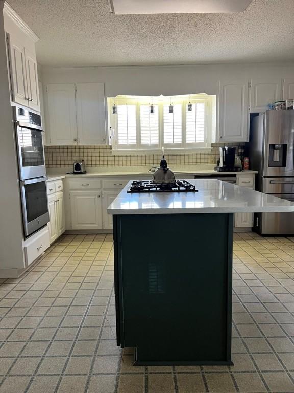 kitchen with decorative backsplash, stainless steel appliances, a kitchen island, and white cabinets