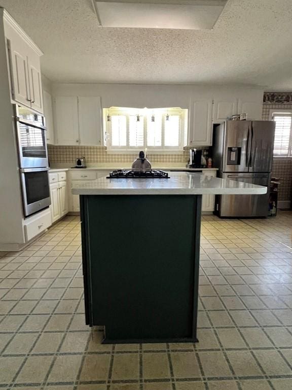 kitchen with light tile patterned floors, a kitchen island, white cabinets, stainless steel appliances, and backsplash