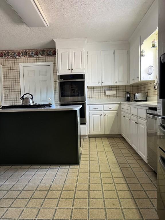 kitchen featuring white cabinetry, stainless steel double oven, tasteful backsplash, and a textured ceiling