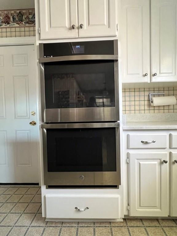 kitchen with white cabinetry, double oven, and backsplash