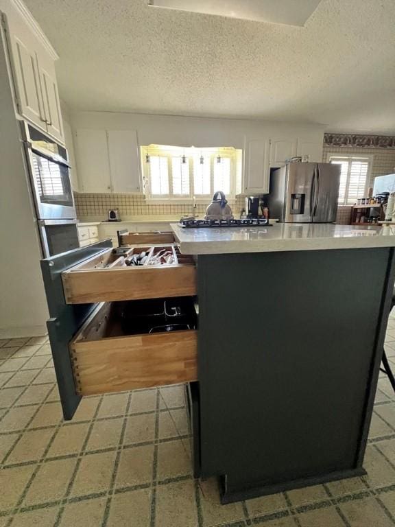 kitchen featuring stainless steel appliances, white cabinetry, backsplash, and a textured ceiling