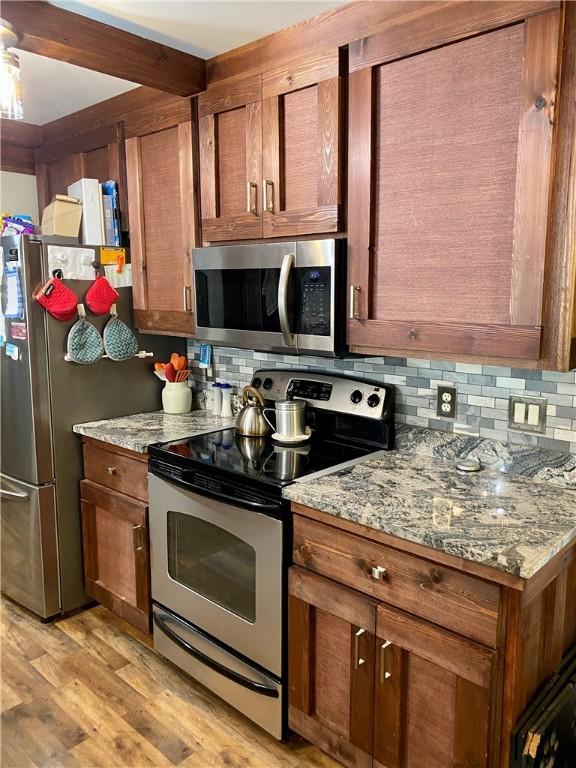 kitchen with tasteful backsplash, appliances with stainless steel finishes, light stone countertops, and light hardwood / wood-style floors