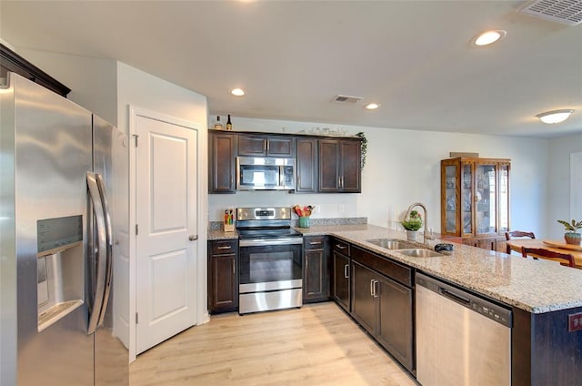 kitchen featuring appliances with stainless steel finishes, sink, light stone counters, kitchen peninsula, and light wood-type flooring