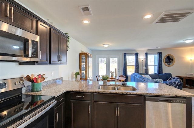 kitchen with appliances with stainless steel finishes, kitchen peninsula, sink, and dark brown cabinets