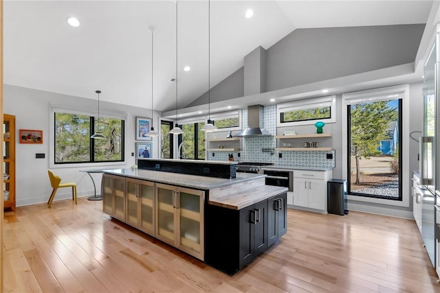 kitchen featuring wall chimney range hood, hanging light fixtures, light stone countertops, white cabinets, and a kitchen island